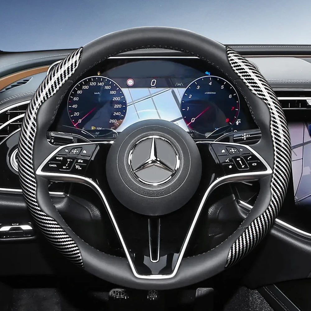 Close-up view of a black steering wheel with carbon fiber texture covers and a Mercedes-Benz logo.