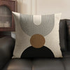 A beige linen cushion cover featuring a geometric design of concentric black lines and a large circular brown shape on a dark