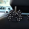 Black bow-shaped car seat back hook with storage attached to a black leather seat.