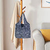A dark blue patterned reusable shopping tote bag hanging on a wooden rack next to a beige towel.