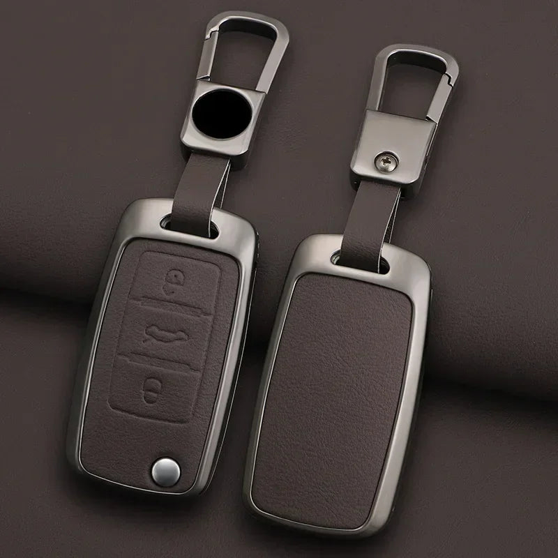 A pair of metallic key case covers with split rings and rectangular key holders resting on a dark surface.