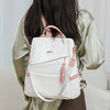 A woman is holding a white vegan leather backpack with pink accents and a laptop compartment.