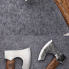 A hand-forged Viking tomahawk axe with a white blade and wooden handle resting on a gray textile surface.