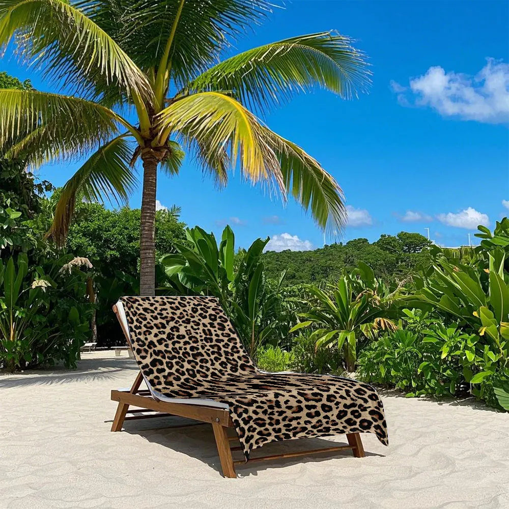 A leopard print quick-dry microfiber towel is displayed on a wooden lounge chair in an outdoor tropical setting.