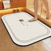 A white diatomite bath mat with a gold trim and a small flower design is placed on a tiled floor.