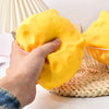 A hand is squeezing a yellow cheese-themed squishy stress relief toy on a woven mat.