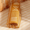 A rolled muslin baby swaddle blanket in mustard yellow with white geometric patterns resting on a light striped surface.