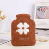A brown plush-covered hot water bottle with white floral embroidery sits next to a book.