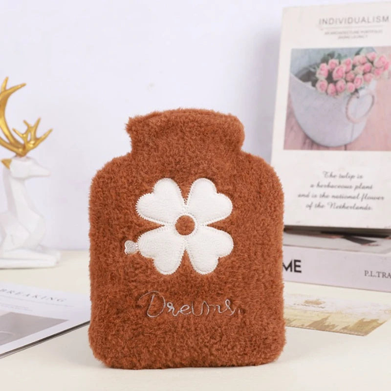 A brown plush-covered hot water bottle with white floral embroidery sits next to a book.