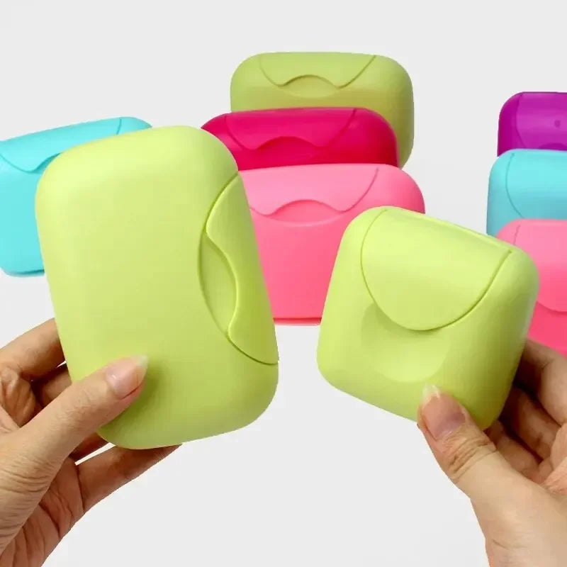 A hand holds a lime green portable soap holder with a lid, surrounded by other colored versions.