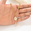 A gold-colored chain necklace featuring a oval pendant with a cross hanging, held in a person's hand.