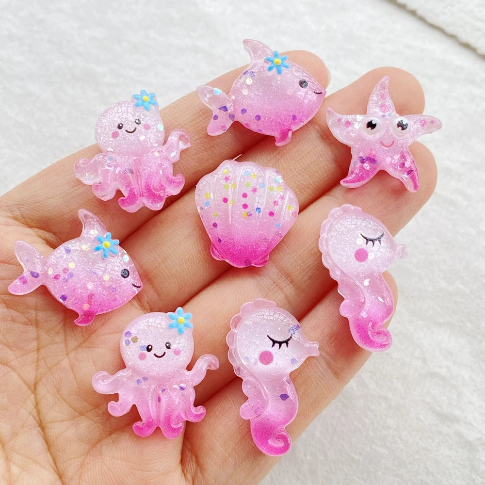 Pink and purple resin sea creature charms shaped like starfish, jellyfish, and small fish held in a hand.