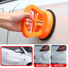 A hand is using an orange heavy-duty suction cup dent puller to lift a car body panel.