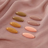 A set of eight classic solid color scarf pins in shades of yellow and pink are displayed on a soft pink fabric.
