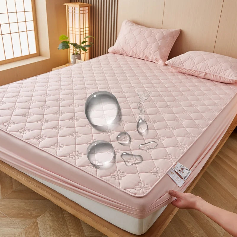 A pink quilted mattress protector is displayed on a wooden bed frame with various clear silicone molds.