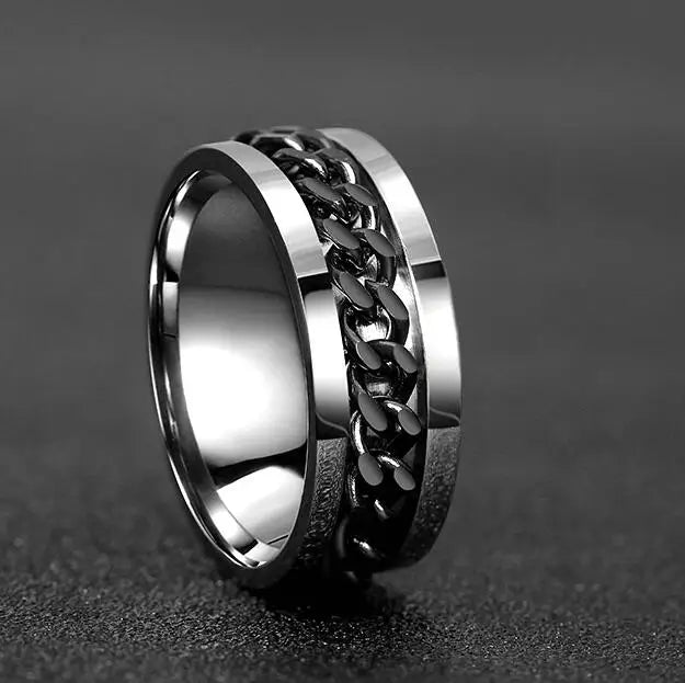 A close-up shot of a stainless steel spinner ring with a textured chain design on a dark surface.