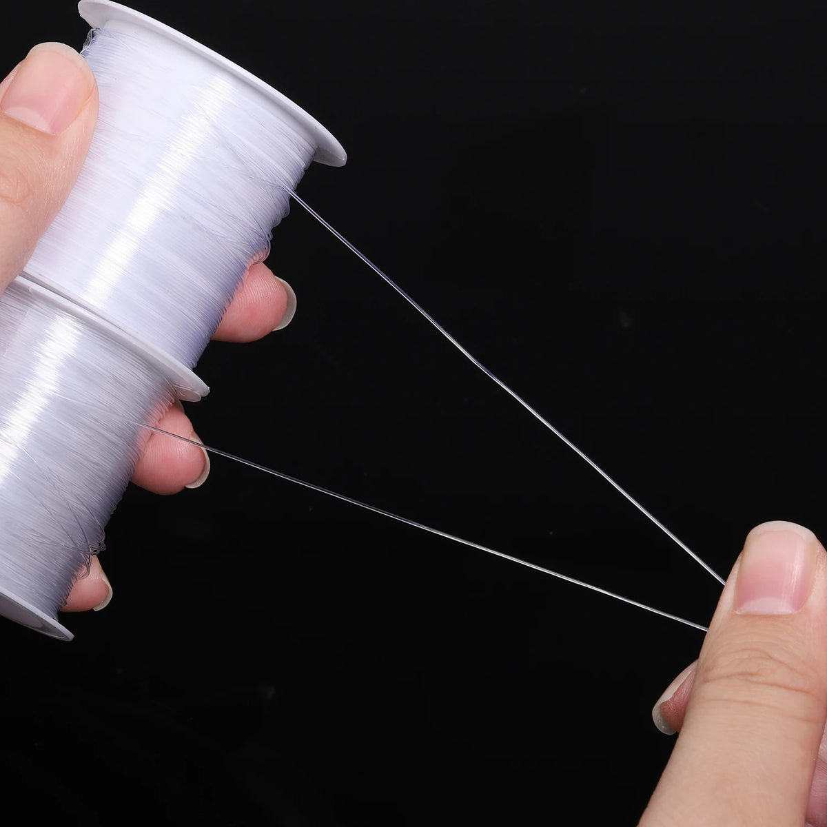 A hand holds a spool of white nylon beading cord, with a thin strand stretched out.