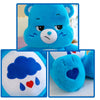 Peluche Kawaii Care Bears arcoíris azul con expresión triste, mostrando primeros planos de su cara y detalle del corazón.
