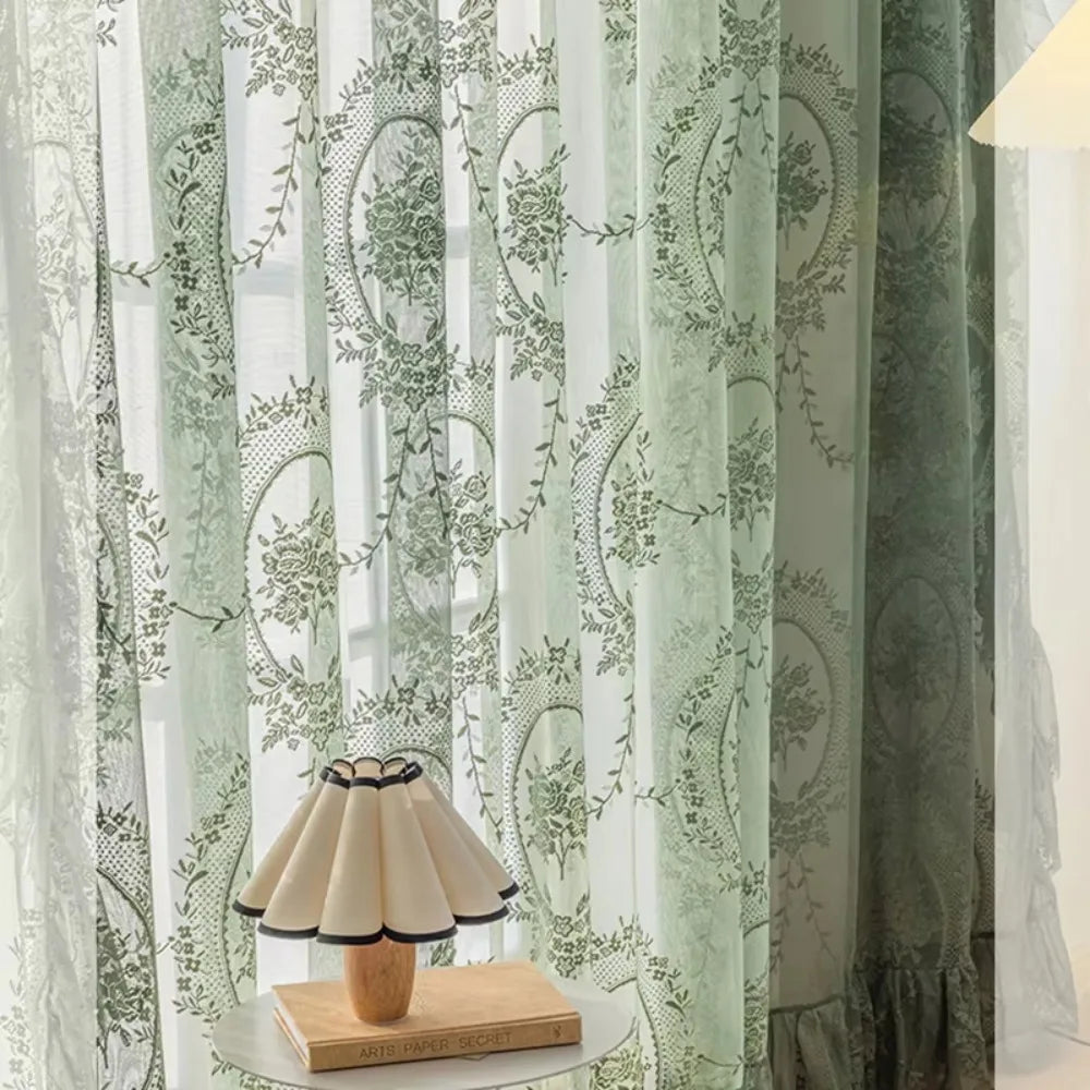 Light green sheer curtains with floral embroidery and ruffled French lace detailing hanging in a window.