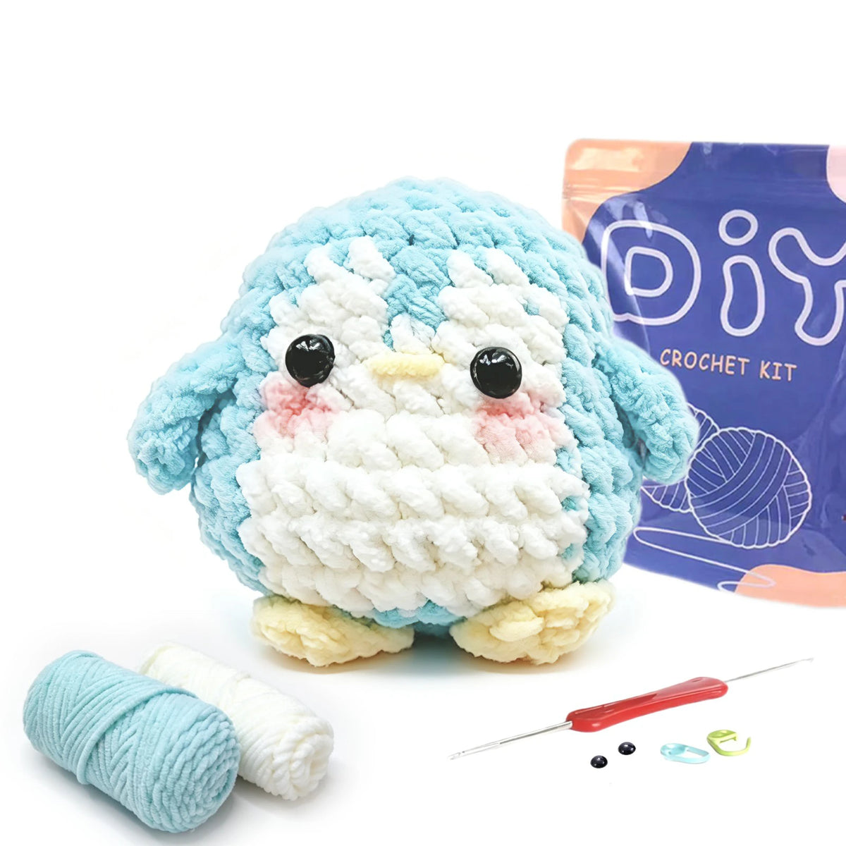 A crocheted blue and white animal figure next to yarn, needles, and small craft items for a beginner crochet kit.
