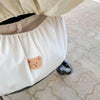 A white fabric stroller organizer featuring a cute bear patch on the side, shown in a close-up view.