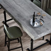 A modern dining table with a gray wood grain surface, featuring a dark bottle and nuts on a silver plate.