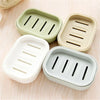 Three silicone soap holders in light green, beige, and white are arranged on a wooden surface.