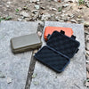 A black waterproof sealed storage box is shown next to an orange box on a gray stone surface.