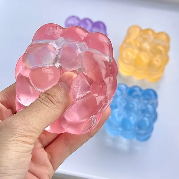Une main tient un cube anti-stress rose et montant lentement, avec des cubes jaunes et bleus.