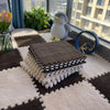 A stack of brown and white interlocking plush floor tiles with a gray stuffed animal on a light rug near a window.