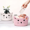 A hand is placing a weekly schedule into a pink woven cotton rope storage basket shaped like a cat.