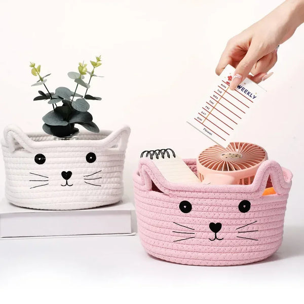 A hand is placing a weekly schedule into a pink woven cotton rope storage basket shaped like a cat.