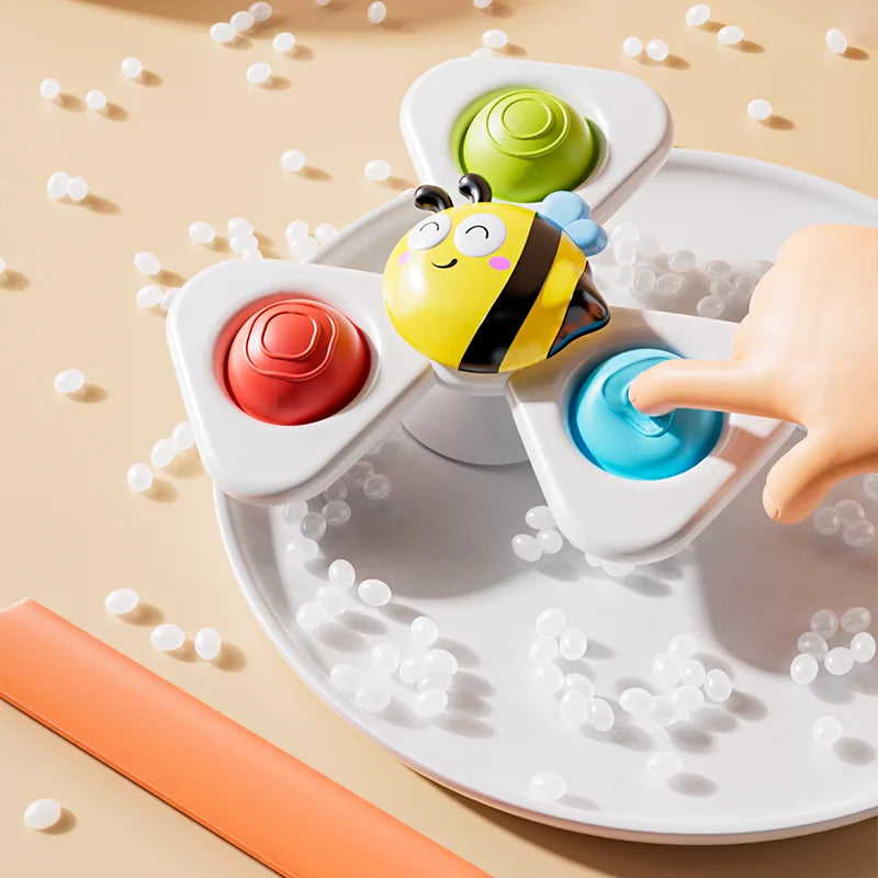A hand is interacting with a spinning bath toy featuring an elephant and bee design on a white tray.