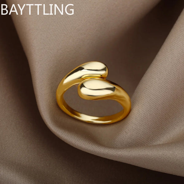 Primer plano de un anillo en forma de gota abierto con detalles dorados sobre tela beige suave.
