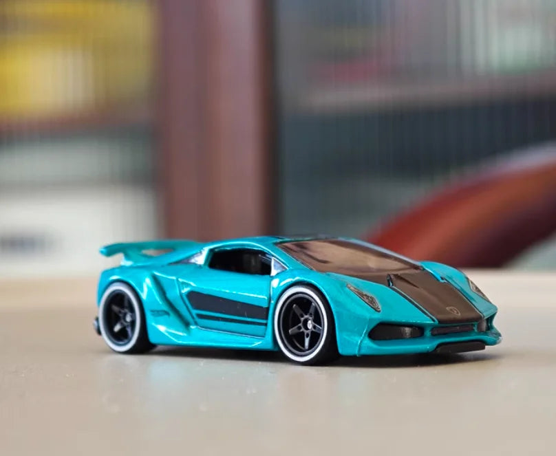 A teal 1:64 scale alloy car model with a black hood and racing wheels on a light surface.