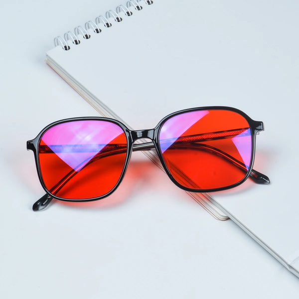 A pair of square red-tinted blue light blocking glasses resting on a white spiral notebook.