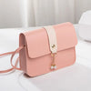 A light pink compact crossbody handbag with a beige adjustable strap and gold chain charm resting on a white surface.