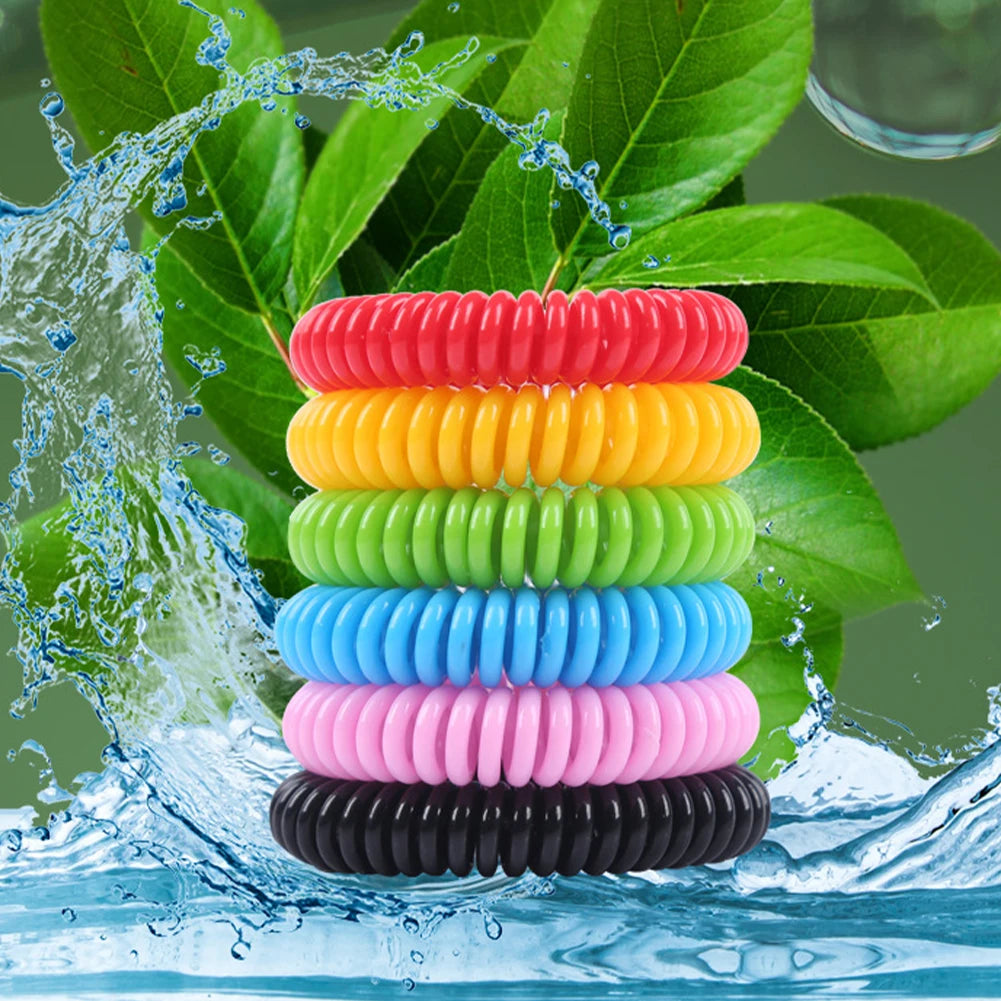 A stack of ten colorful silicone bracelets in rainbow order being washed by water amidst green leaves.