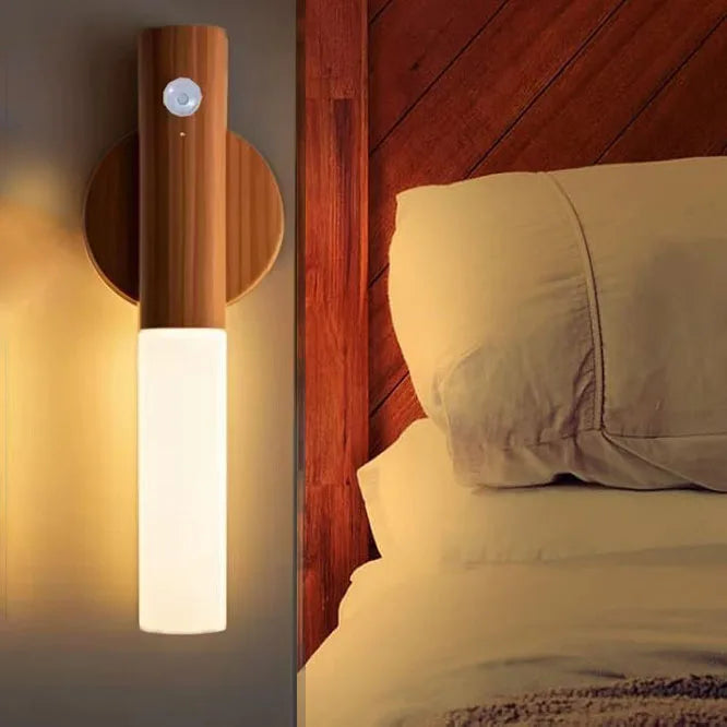 A modern magnetic LED wall light with a motion sensor mounted on a wooden panel next to a bed.