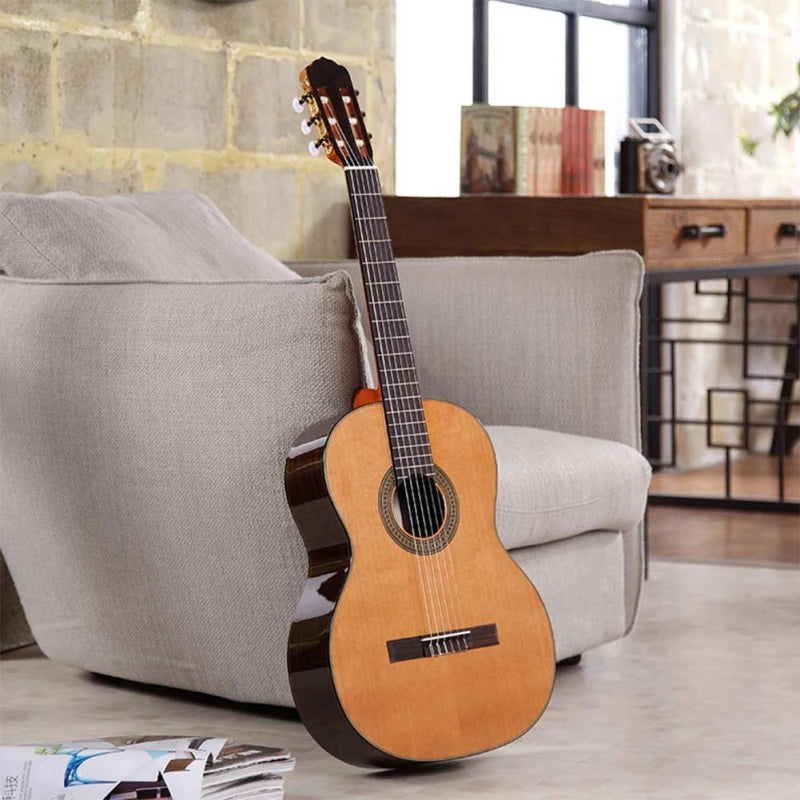 A wooden classical guitar is resting on a light gray sofa in a well-lit room.