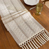 Beige boho table runner with tassels hand-woven farmhouse style placed on a wooden table.