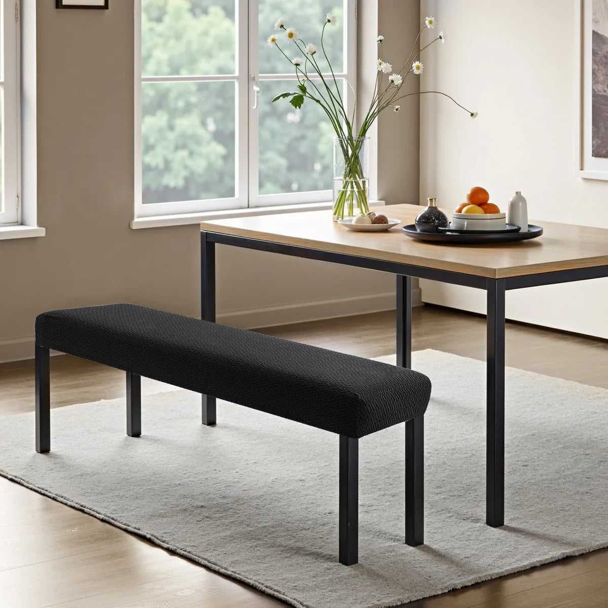 A black stretch jacquard bench cover is shown on a wooden table in a bright room.