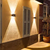 A solar powered LED wall light illuminates a textured wall with upward and downward beams.