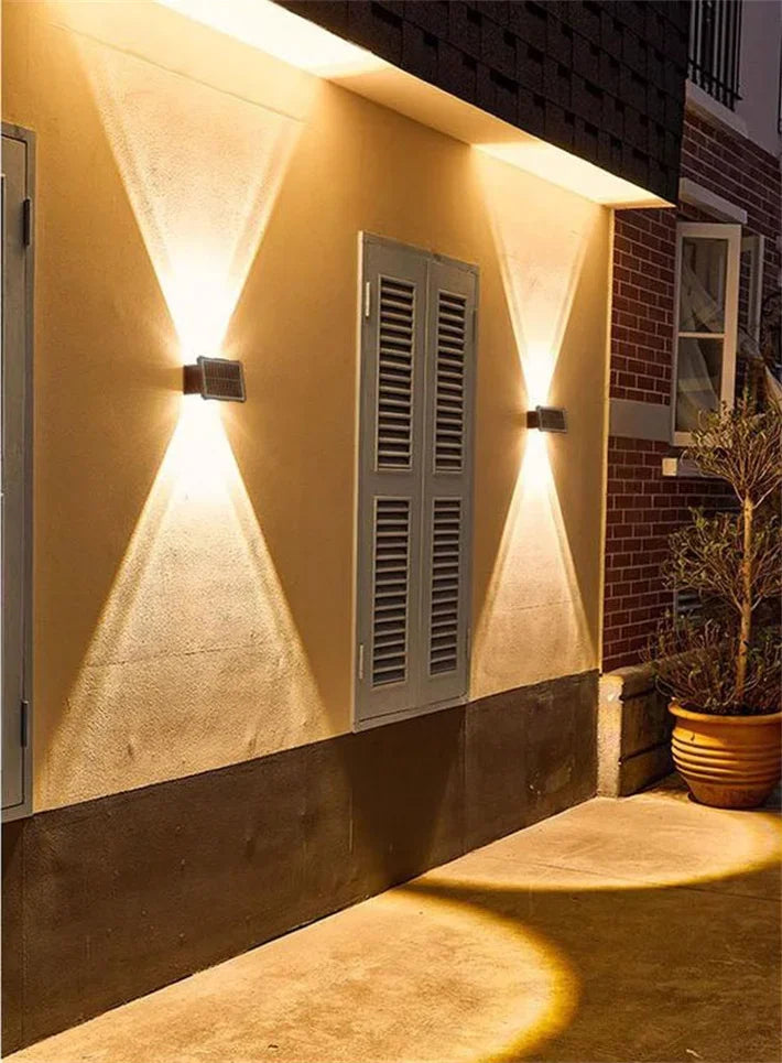 A solar powered LED wall light illuminates a textured wall with upward and downward beams.