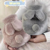 A soft pink plush rabbit hot water bottle with a gray flannel cover being held in a person's hands.