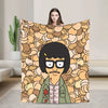 A person holds up a throw blanket featuring a cartoon character with black hair and glasses against a patterned background.