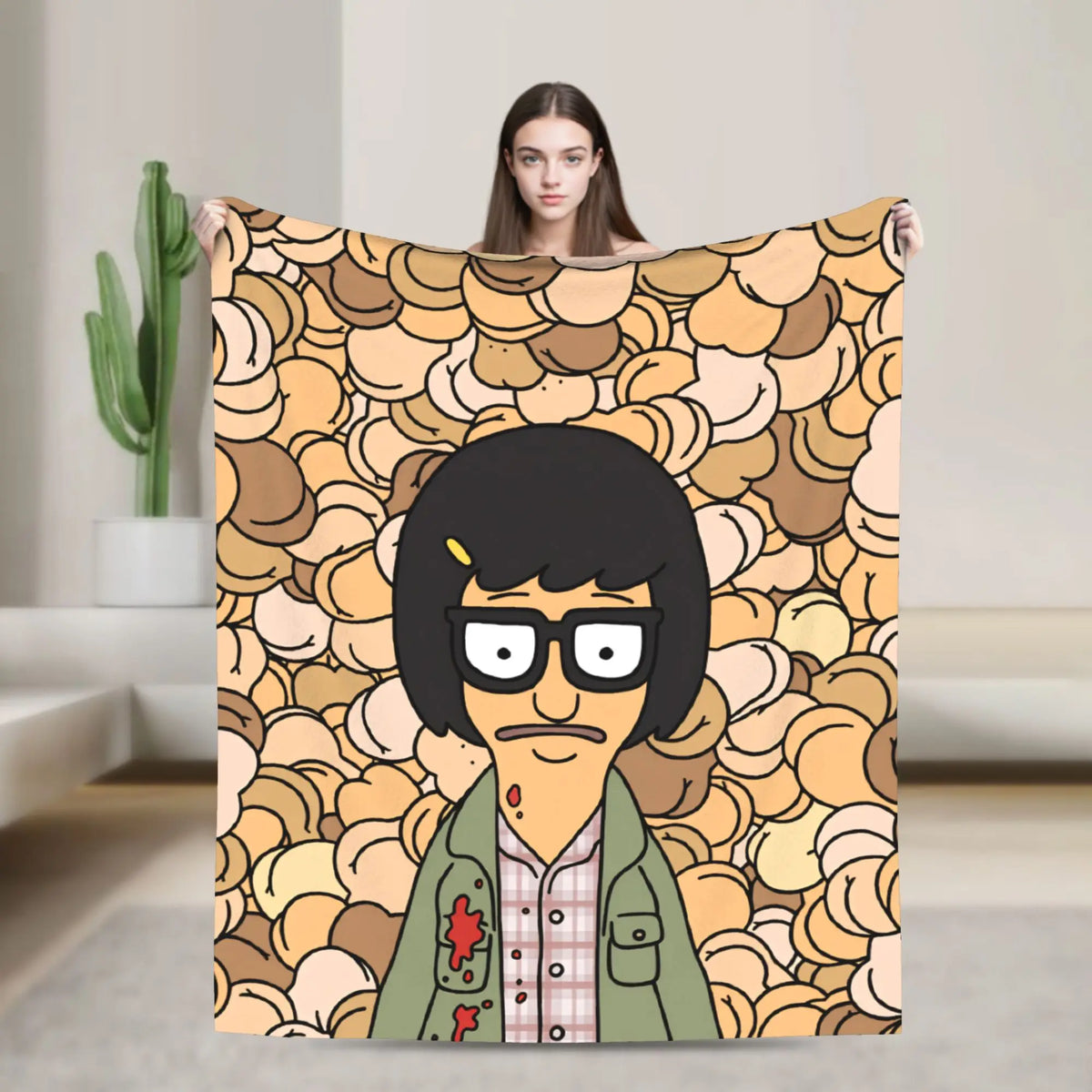 A person holds up a throw blanket featuring a cartoon character with black hair and glasses against a patterned background.