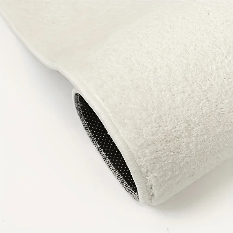 A close-up view of a thick, off-white plush non-slip rug or mat with a black edge.