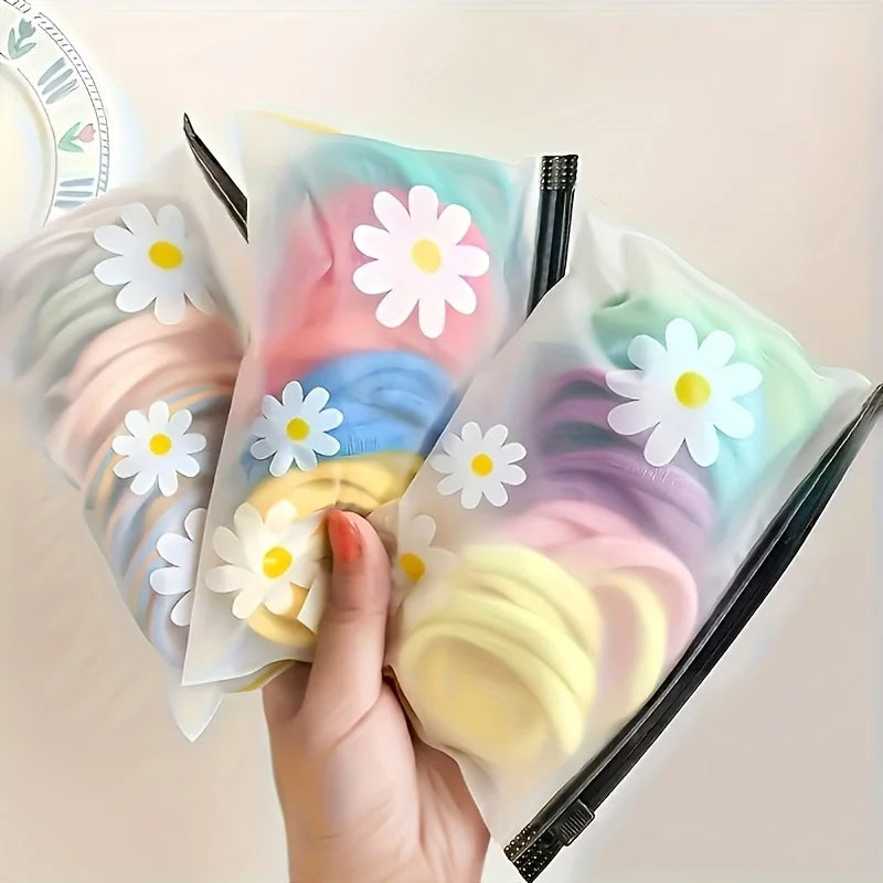 A hand holds a set of ten frosted zipper bags with a daisy pattern, showing various pastel colors.
