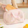 A pink quilted insulated lunch tote is shown next to a wooden lid, with a person's hand holding the item.
